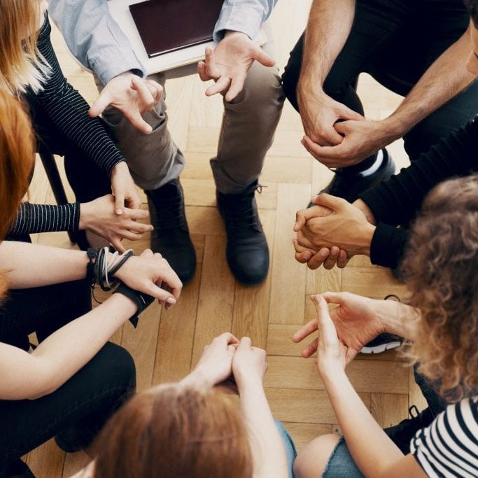 Close-up of hands of teenagers sitting in a circle during a support meeting
